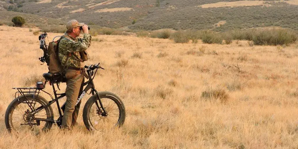 A man in camouflage on an electric bike looking through binoculars.