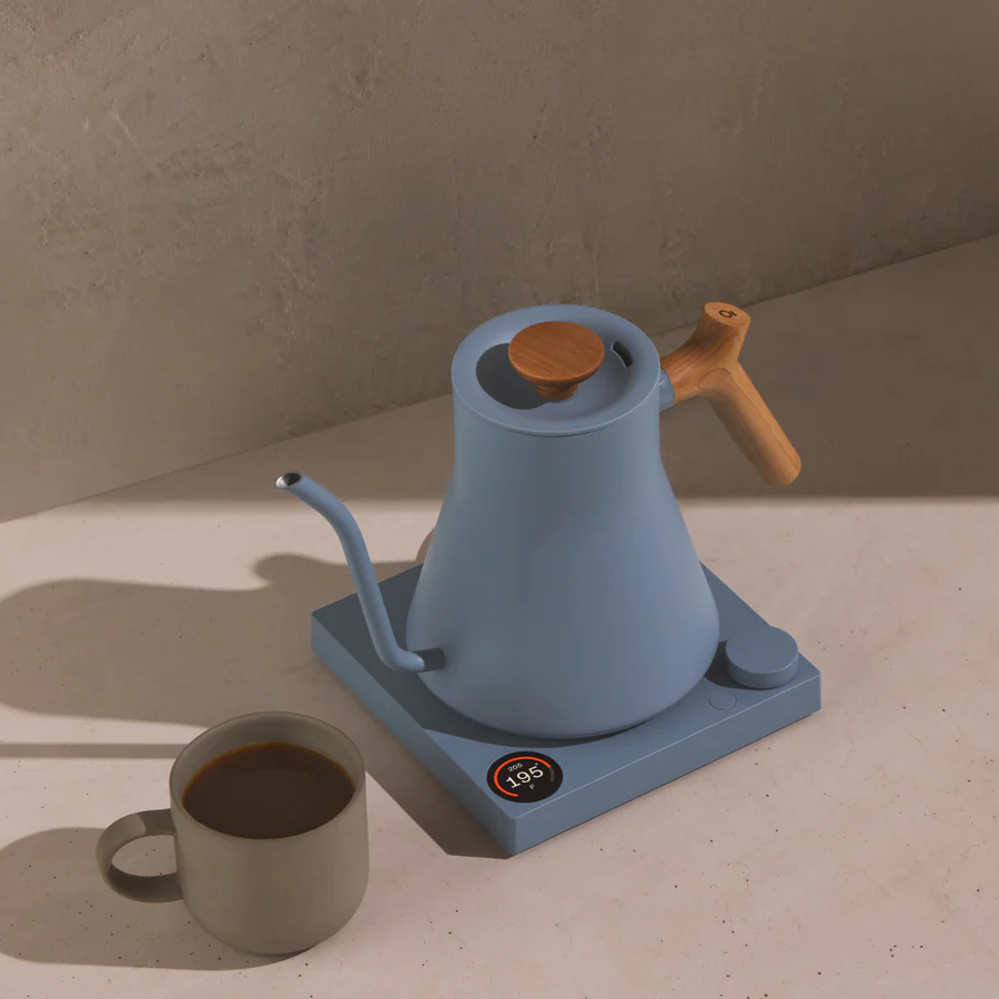 A blue, modern-looking electric kettle next to a mug of tea.