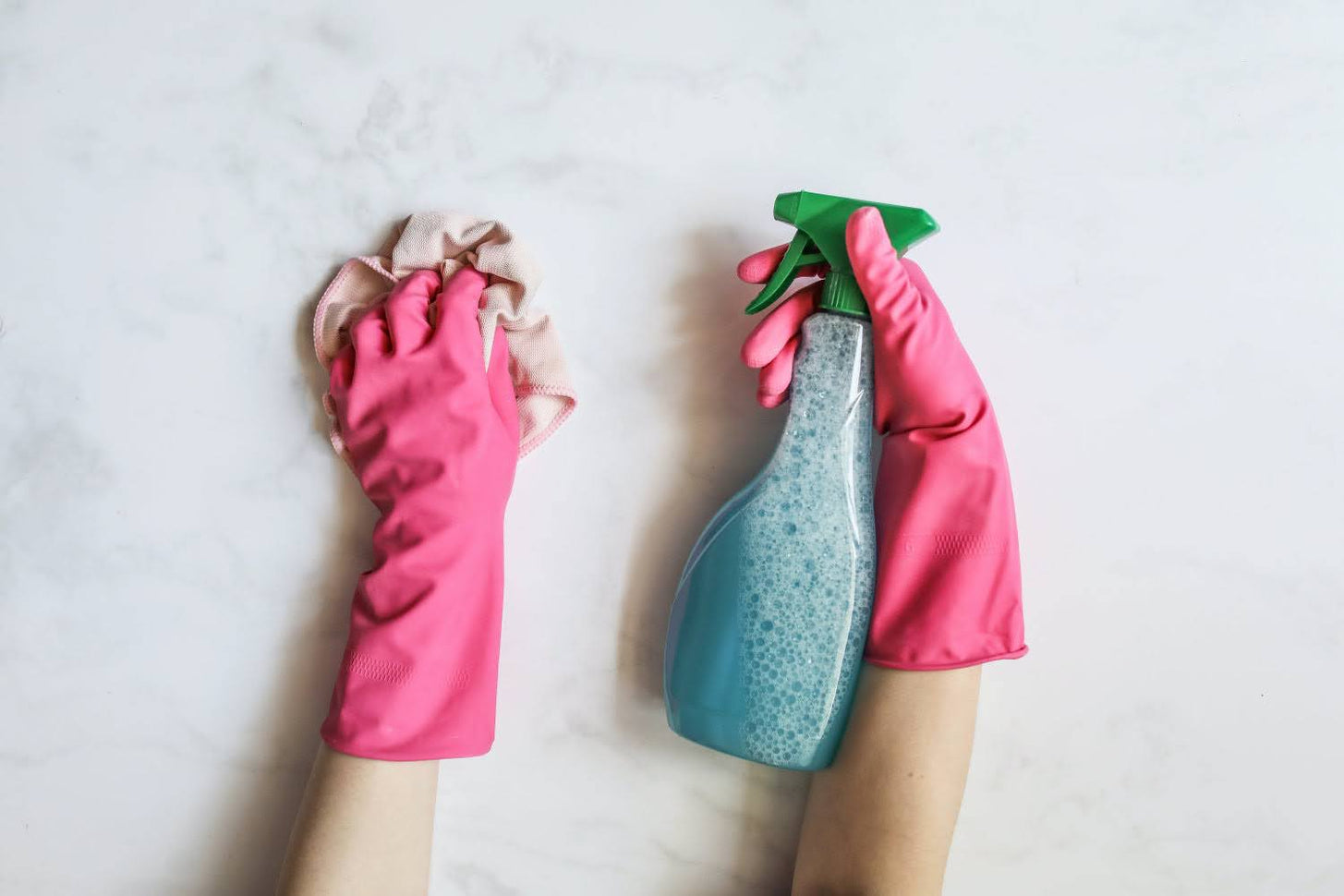 A pair of hands wearing cleaning rubber gloves and holding a rag and spray bottle